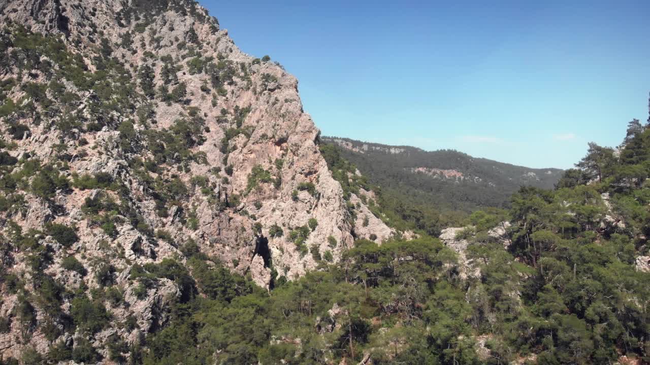 巨大的岩石山峰与松树和云杉森林对着清澈的蓝天。在晴朗的夏日飞越高山。冒险旅行的概念。野生自然景观视频素材