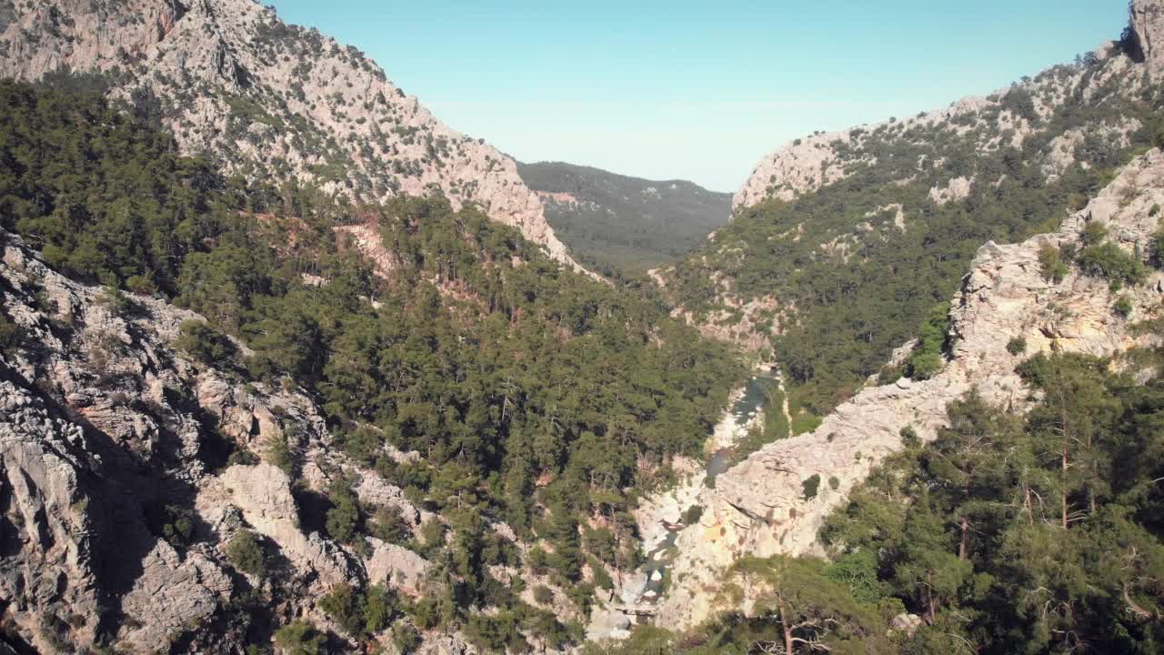 阳光明媚的夏日，美丽的高海拔山脉。绿色的森林树木在岩石山上映衬着清澈的蓝天。飞过群山和岩石峭壁之间的巨大峡谷。野生自然视频素材