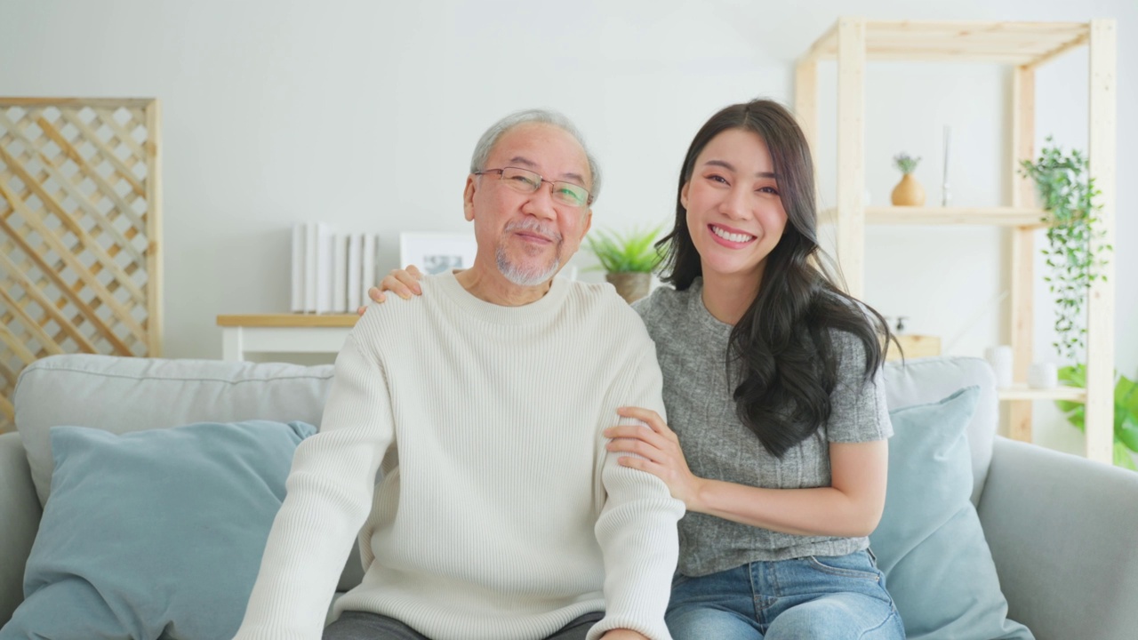 亚洲女儿的肖像拜访年长的父亲，一起看电影。年长的爷爷和美丽的女孩孙女坐在沙发上欣赏电视上的喜剧节目，花时间在客厅。视频素材