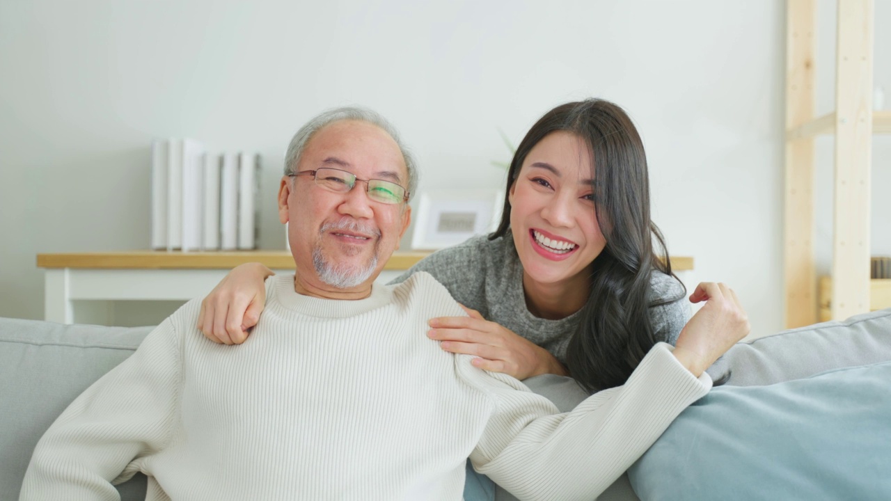 可爱的亚洲家庭，年轻的女儿问候并拥抱年长的父亲。迷人的女人孙女拜访老人成熟的男人在家里享受在客厅一起度过休闲时间和微笑。视频素材