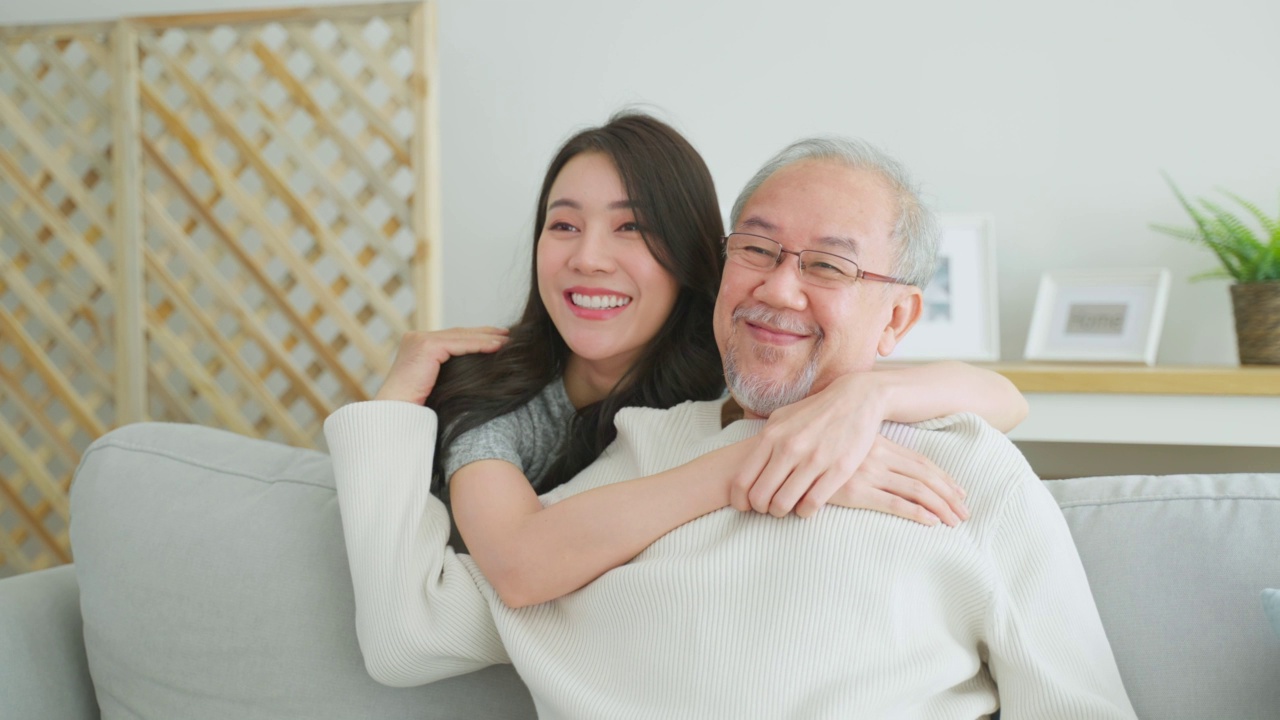 可爱的亚洲家庭，年轻的女儿问候并拥抱年长的父亲。迷人的女人孙女拜访老人成熟的男人在家里享受在客厅一起度过休闲时间和微笑。视频素材