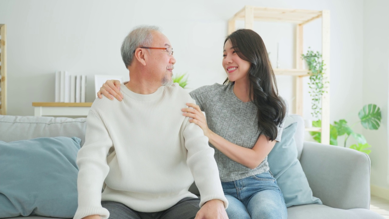 亚洲女儿的肖像拜访年长的父亲，一起看电影。年长的爷爷和美丽的女孩孙女坐在沙发上欣赏电视上的喜剧节目，花时间在客厅。视频素材