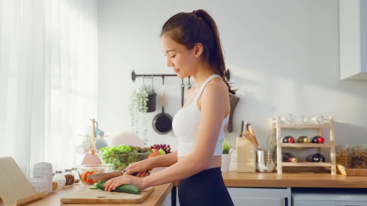 两个穿着运动服的亚洲年轻女子在厨房里做沙拉。活泼漂亮的女孩姐姐感到快乐，喜欢吃蔬菜健康的食物来减肥，在家里的保健视频素材