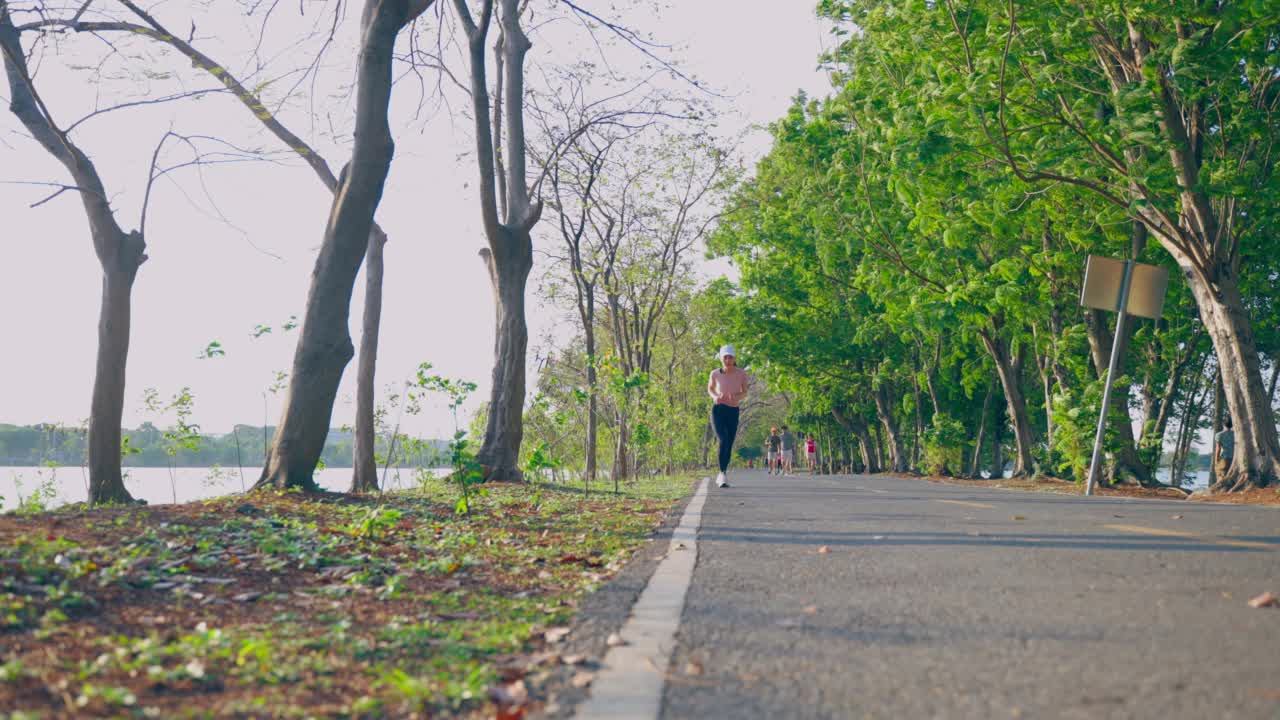 亚洲年轻美丽的运动女子在公共公园的街道上跑步。美丽的运动员，健美和坚定的女孩在运动服装锻炼慢跑，户外锻炼，在傍晚，在花园的保健。视频素材