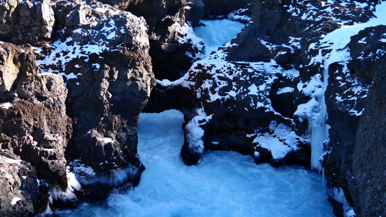 在阳光明媚的冬天，冰岛Hraunfossar瀑布附近的峡谷中的Barnafoss瀑布，Húsafell，自然岩石拱门，汹涌的河流和冰的形成。视频素材