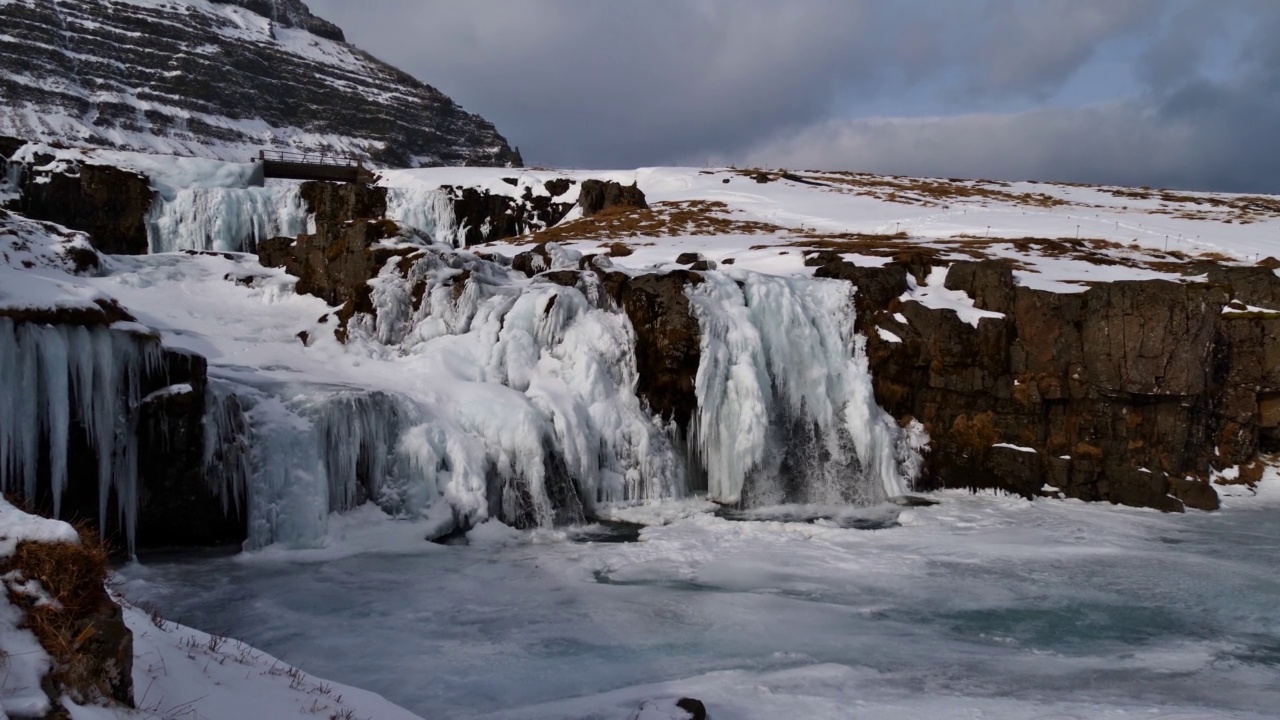 在冰岛西部Snæfellsnes半岛Grundarfjörður附近冰冻的岩石Kirkjufellsfoss瀑布，冬季有雪，冰的形成和冰柱。视频素材