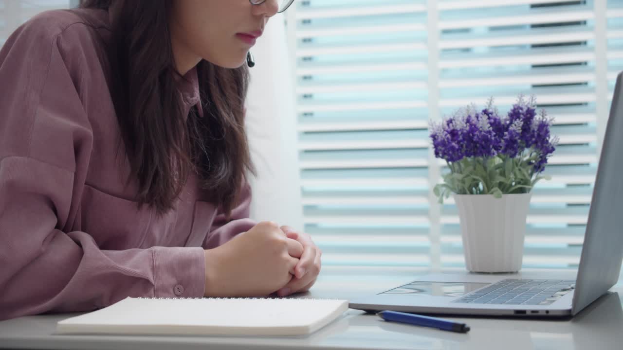 亚洲女学生在家桌上用笔记本电脑在线学习。女性戴着耳机，看着笔记本电脑说话，解释和写笔记。在家学习。在线学习的概念。视频素材