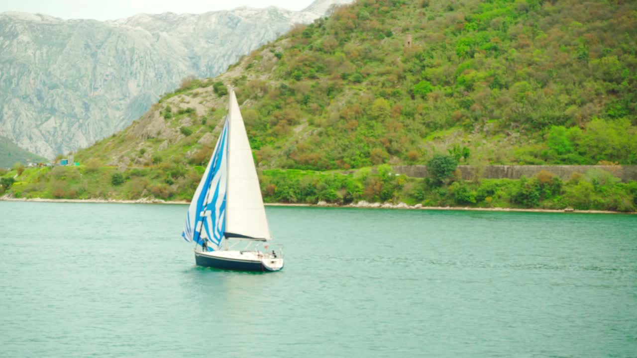 夏日里，一艘帆船在群山的映衬下漂浮在海面上视频素材