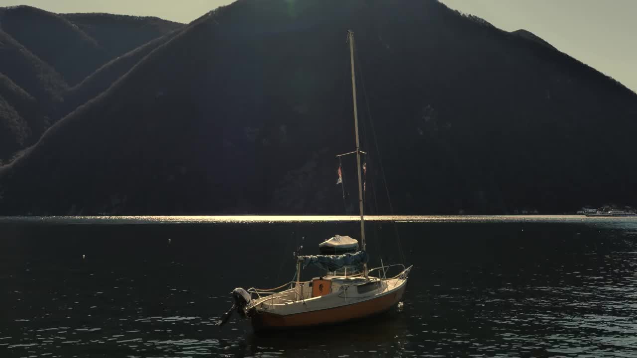 阳光明媚的日子里，有山的卢加诺湖上的帆船和客船视频素材