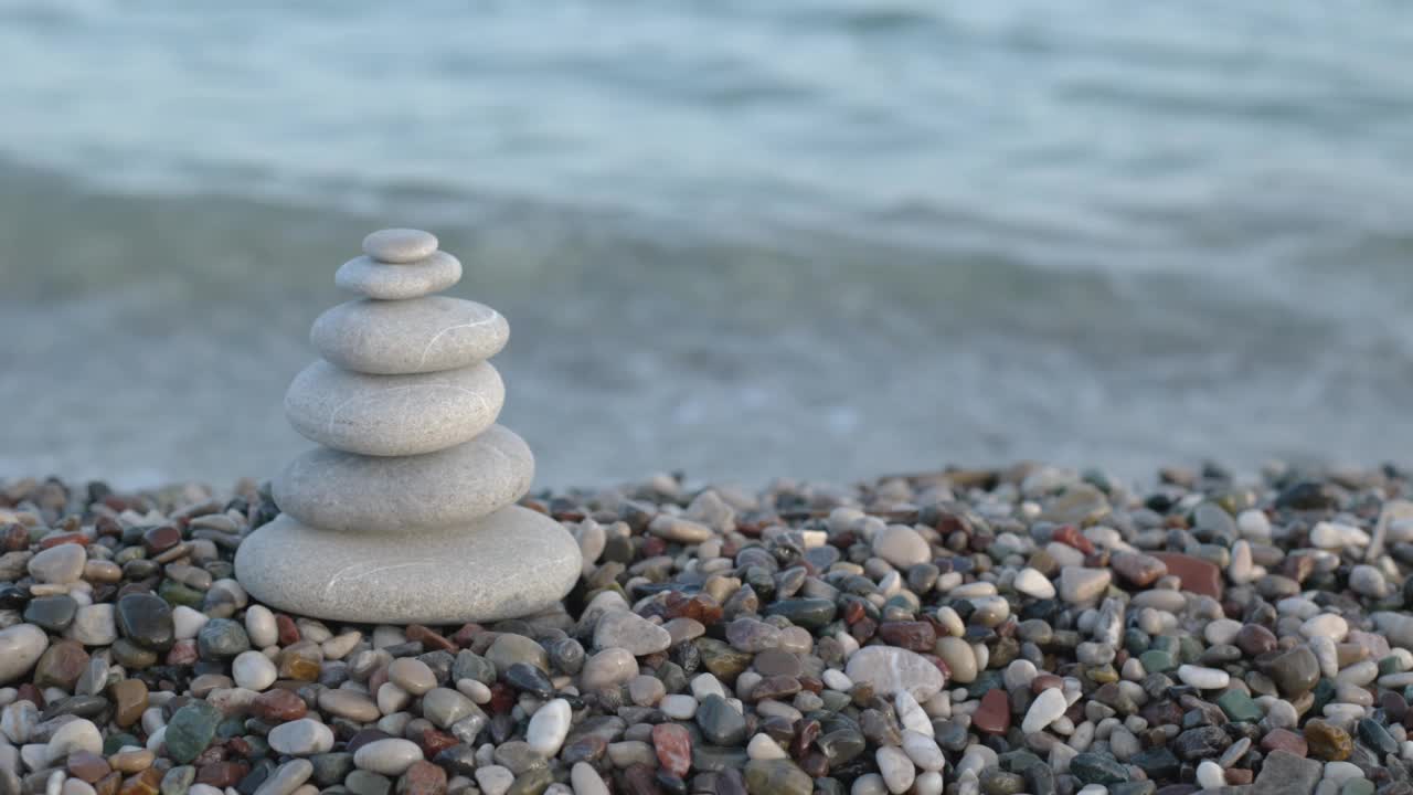 一堆堆石头堆在卵石滩上，在海浪中摇曳。冷静的概念视频素材