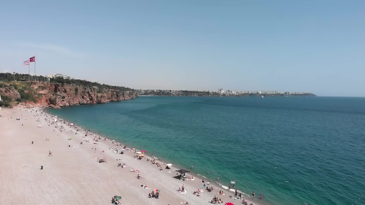 阳光明媚的夏天，海岸线上有山峦和卵石滩。游客们在炎热的夏天在海滩上晒日光浴和放松。夏季海滩度假概念。热带旅游目的地视频素材