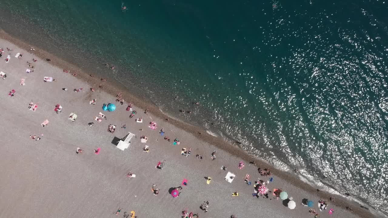 地中海狭长的卵石滩。夏季海滩度假概念。沙滩上的休闲娱乐活动。人们躺在沙滩上撑着伞，游泳，晒日光浴，享受炎热的夏天视频素材