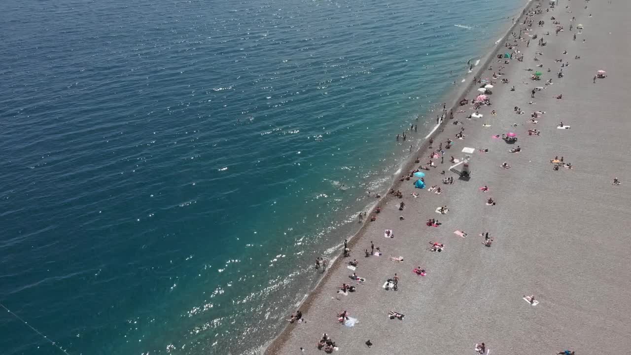 人们在海滩。游客们在地中海海岸的沙滩上乘凉，躺在阳伞下，游泳，日光浴，享受夏日假期的周末。沙滩康乐活动视频素材