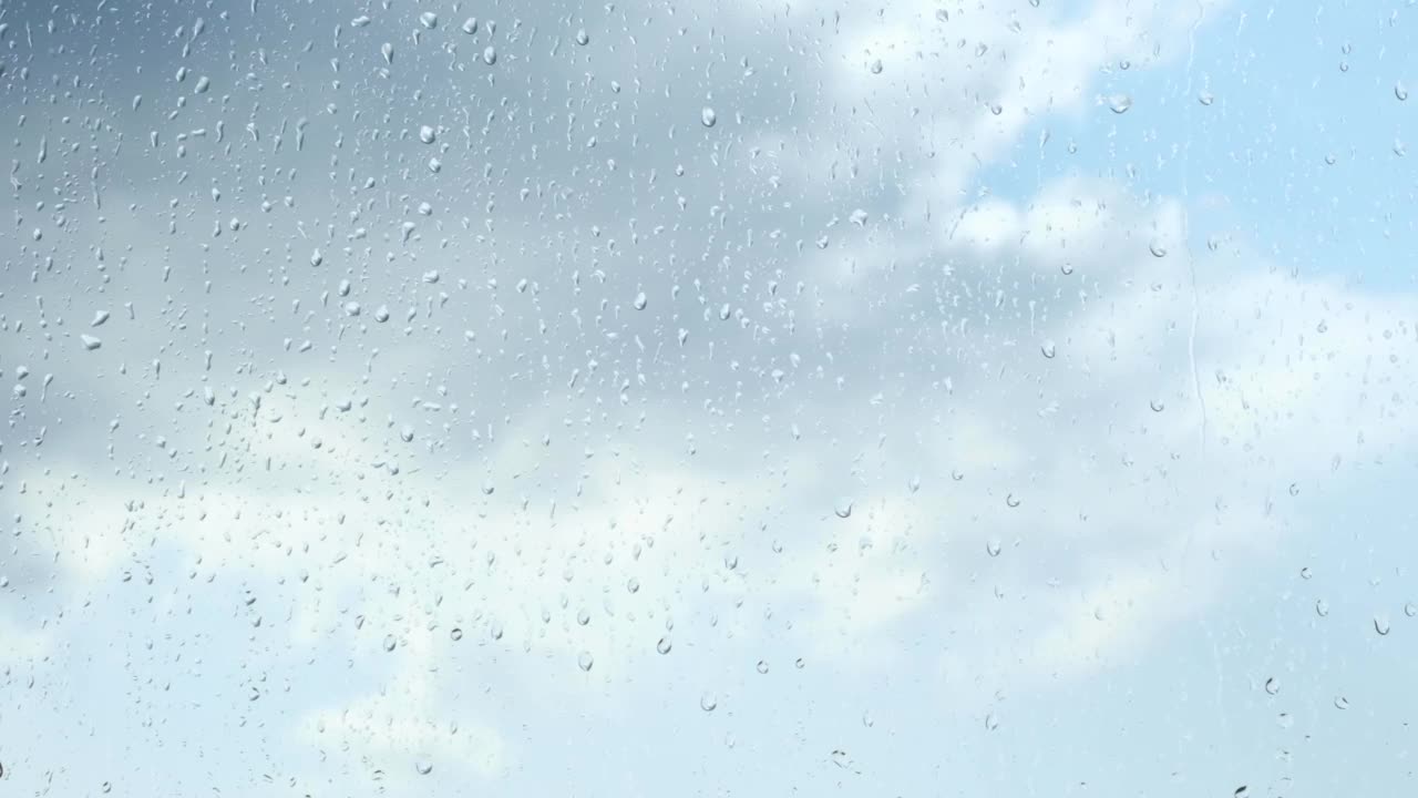 多云的天空下，雨滴落在窗户表面。溪水顺着玻璃流了下来，拉近了距离。视频素材