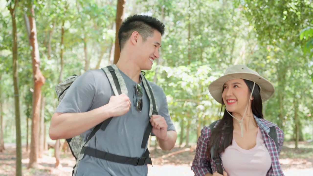 亚洲男人和女人背包客朋友一起在森林里旅行。迷人的年轻夫妇在夏天的假期旅行中散步和探索自然木材的幸福和乐趣。视频素材