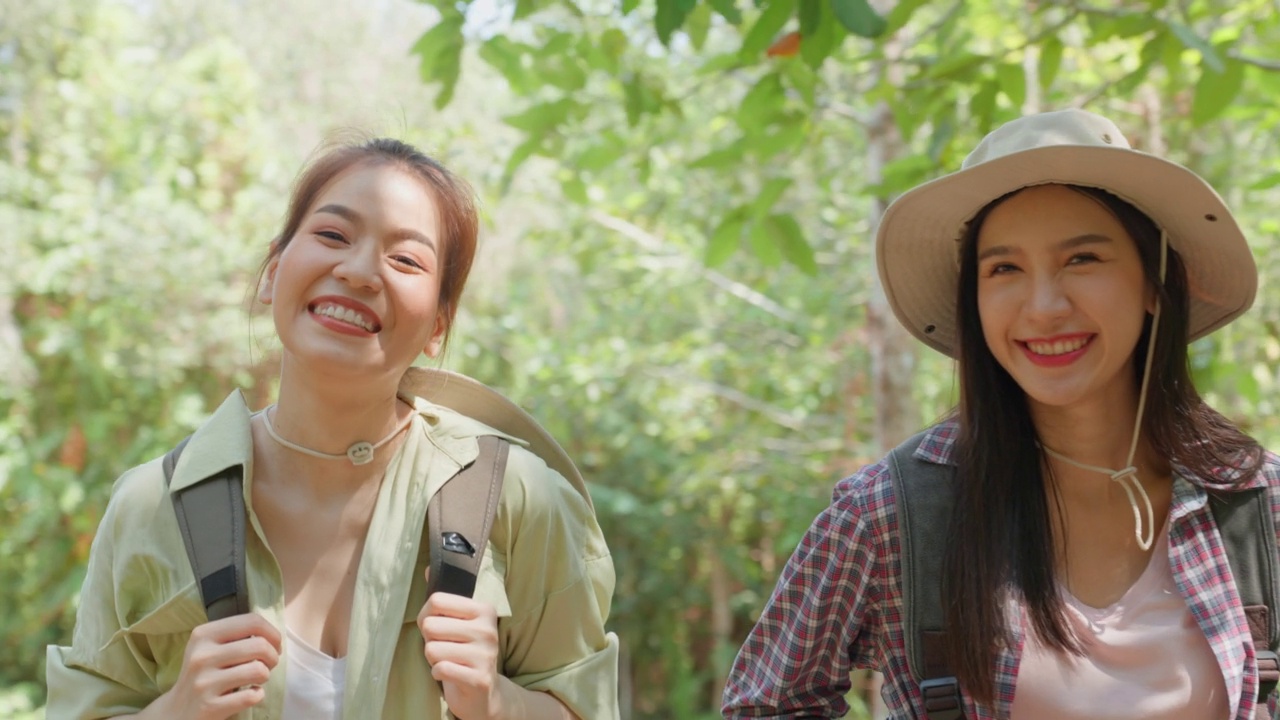 亚洲美丽的两个女人背包旅行在森林野生一起。迷人的年轻女性朋友们在夏天的假期旅行期间散步和探索自然树林的快乐。视频素材