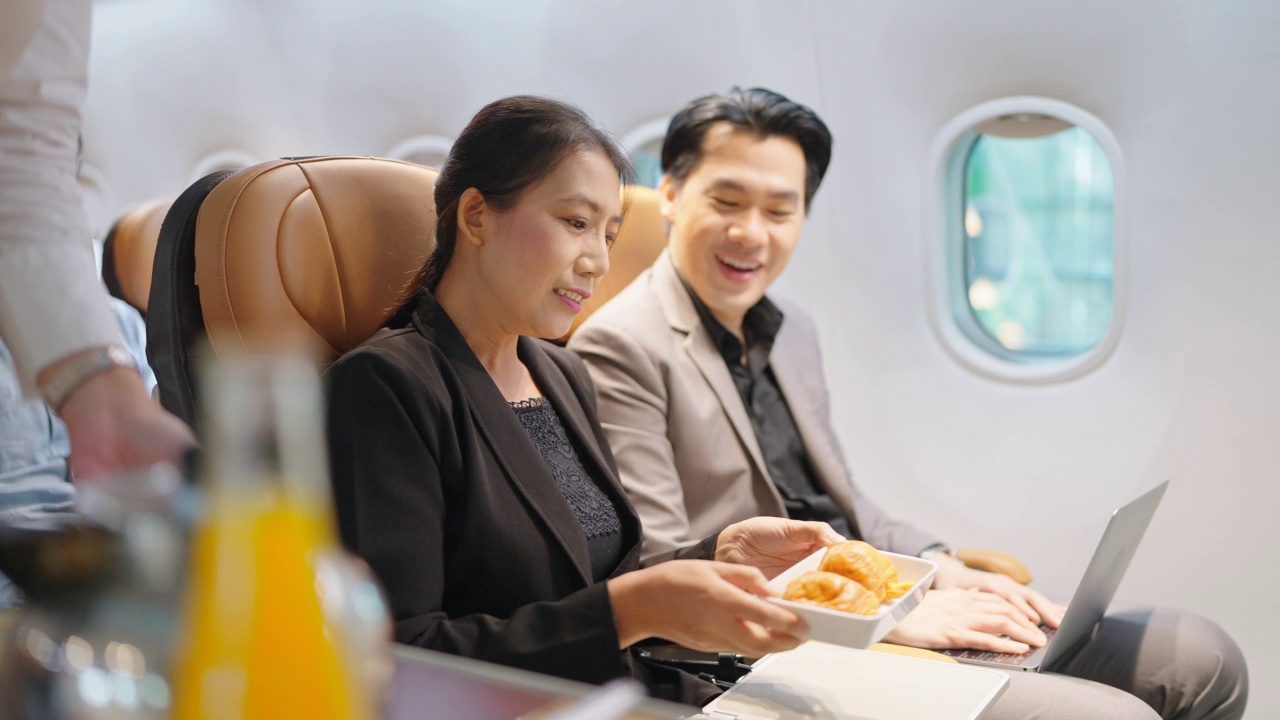 友善的亚洲女空姐在飞机上为乘客提供食物、饮料和交谈。航空公司服务。视频素材