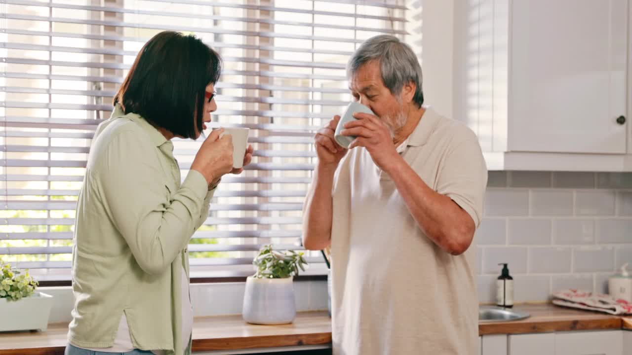 一对亚洲老夫妇一起站在厨房里，享受着一杯茶。老亚洲夫妇喝一杯茶在早上视频素材