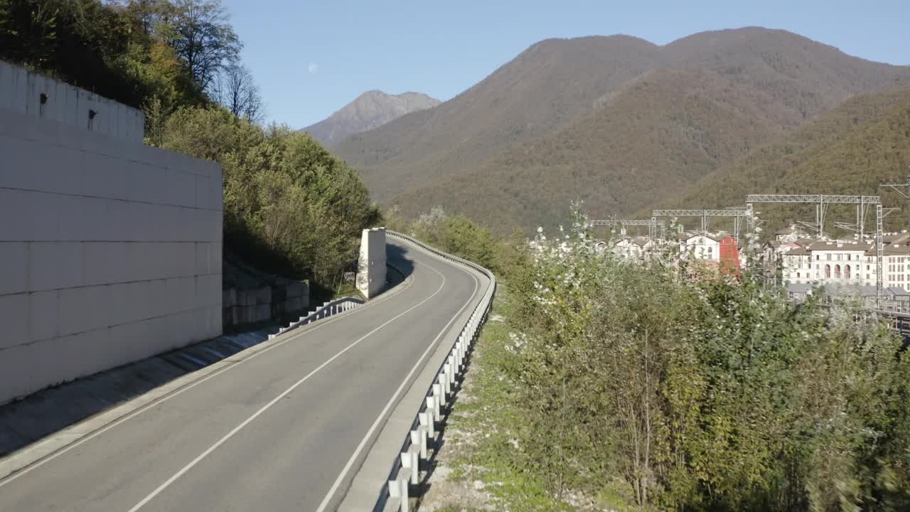 黑色面包车在汽车交通沥青山路上行驶，令人惊叹的全景阳光明媚的豪华度假村村庄的城市景观。鸟瞰图汽车巴士乘坐在蜿蜒的山路山上视频素材