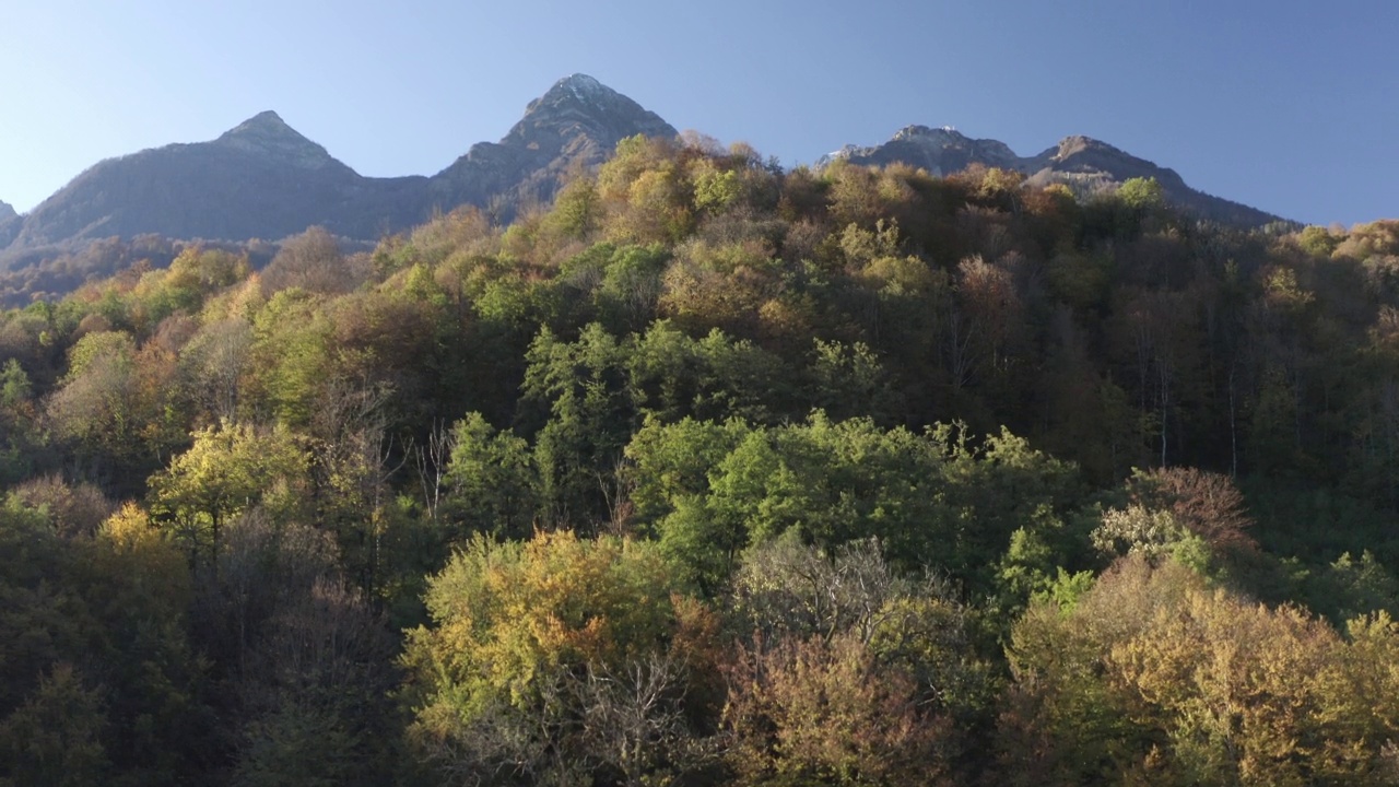 鸟瞰图，在美丽的自然阳光明媚的山区景观村庄度假村地标。从直升机拍摄惊人的自然风光，岩石地形覆盖着绿色的树木，悬崖，雪峰视频素材