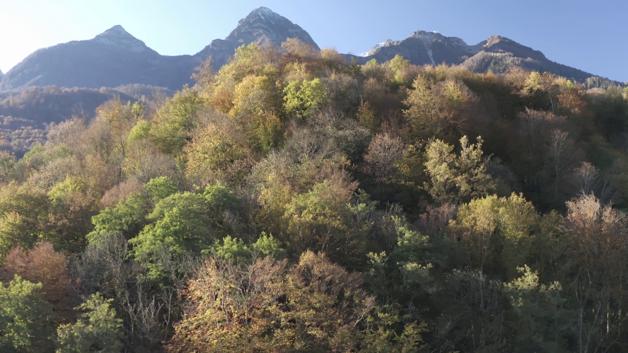 鸟瞰美丽自然阳光明媚的山景村度假地标。从无人机拍摄惊人的自然风景岩石地形覆盖绿色的树木悬崖雪峰在4k视频素材