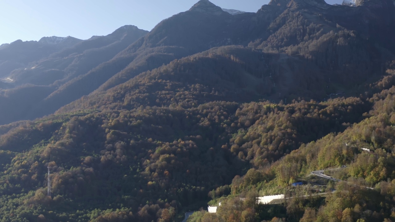 鸟瞰美丽自然阳光明媚的山林景观村度假地标。从无人机拍摄惊人的风景岩石地形覆盖绿色的树木悬崖雪峰在4k视频素材