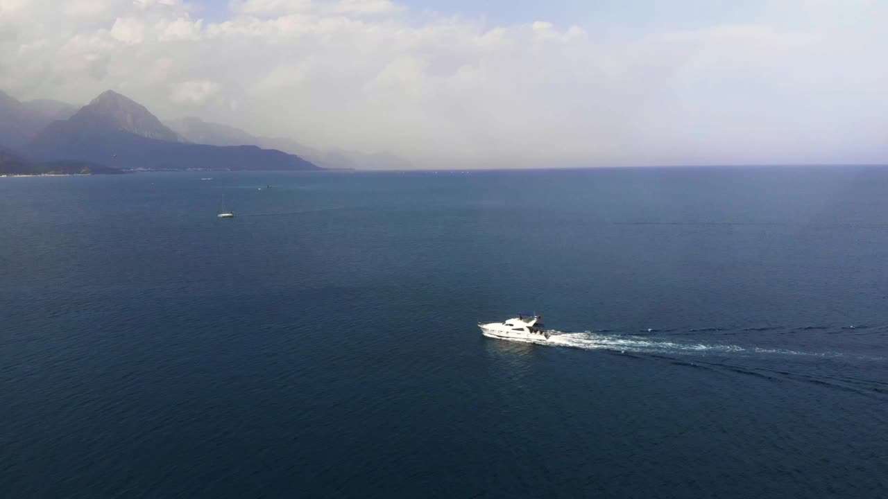 夏天，豪华的白色快艇漂浮在开阔的海面上。在炎热的夏天在海上航行的旅游游艇。人们乘船沿着岩石山脉的海岸线航行。夏天的地中海海滨视频素材