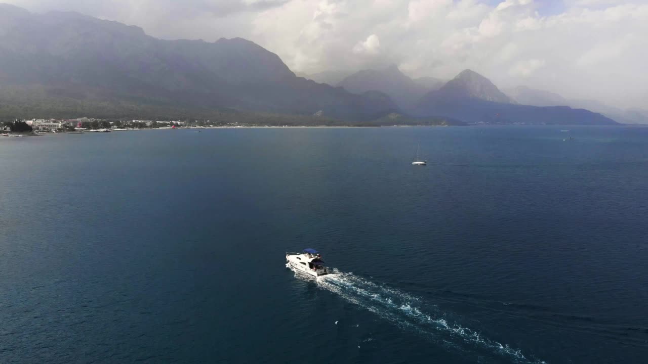 巡航速度船浮动在海上沿岩石山脉的地中海海岸线。白色豪华游艇在平静的海面上航行。夏季休闲活动。旅游度假的概念视频素材