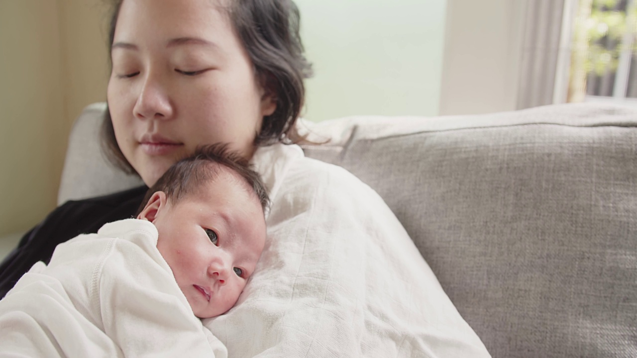 幸福家庭亚洲妈妈抱着新生儿爱抚拥抱婴儿，妈妈的手被打饱嗝，拍揉孩子的背，鼓励孩子吃饱牛奶后打饱嗝，为人父母，爱视频素材