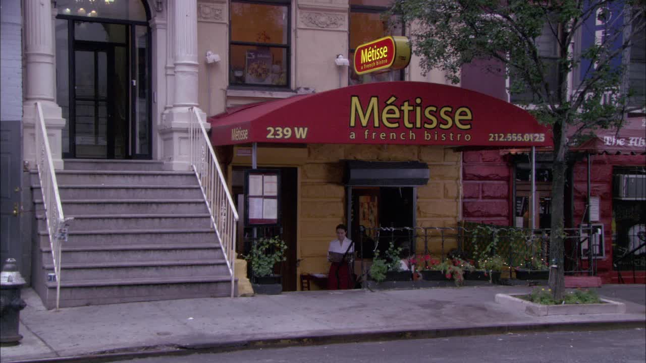 红色遮阳篷和砖外墙的餐厅广角。遮阳篷上写着“metisse a French bistro”。餐厅在曼哈顿的上西区。女主人的门。两个男人走出餐馆。女人经过。视频素材