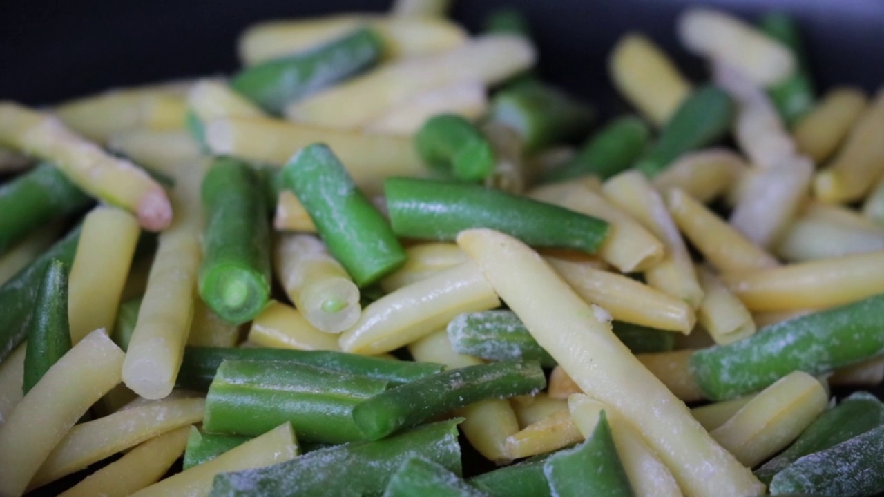 在平底锅里煮鲜芦笋豆。冷冻的绿色和黄色的有机豆茎。冷冻食品的概念视频素材