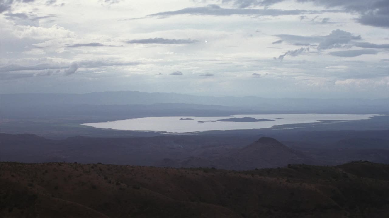 中等角度的山峰和山谷下面和云上面。湖泊在最左边的背景，草原或平原在右边的前景。视频素材