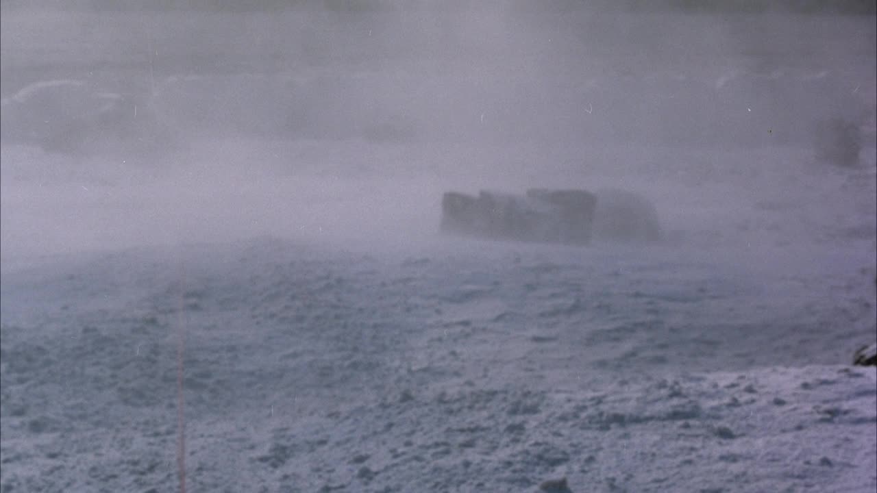 暴雪中大雪覆盖的地面。背景中隐约可见雪中巨石的阴影。向下滑行到红绳垂直穿过pov站在雪和震动上。看到登山者被绳子拉着穿过雪地离开pov。行动。视频素材