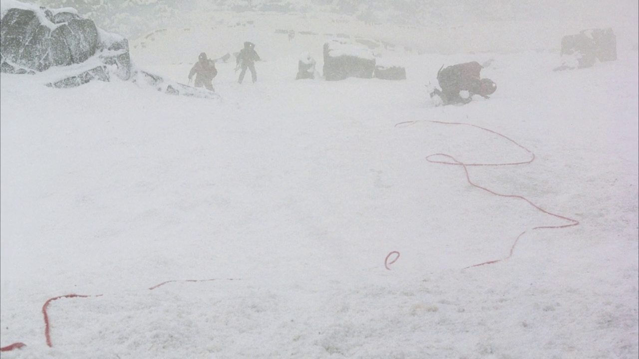 中等角度的登山者徒步穿越暴风雪或暴风雪。看到第一个徒步者或攀登者双膝着地，背对pov。看到红色的绳子卷向左边。绳索拉紧，第一个徒步旅行者向后拉，胳膊和腿乱蹬视频素材