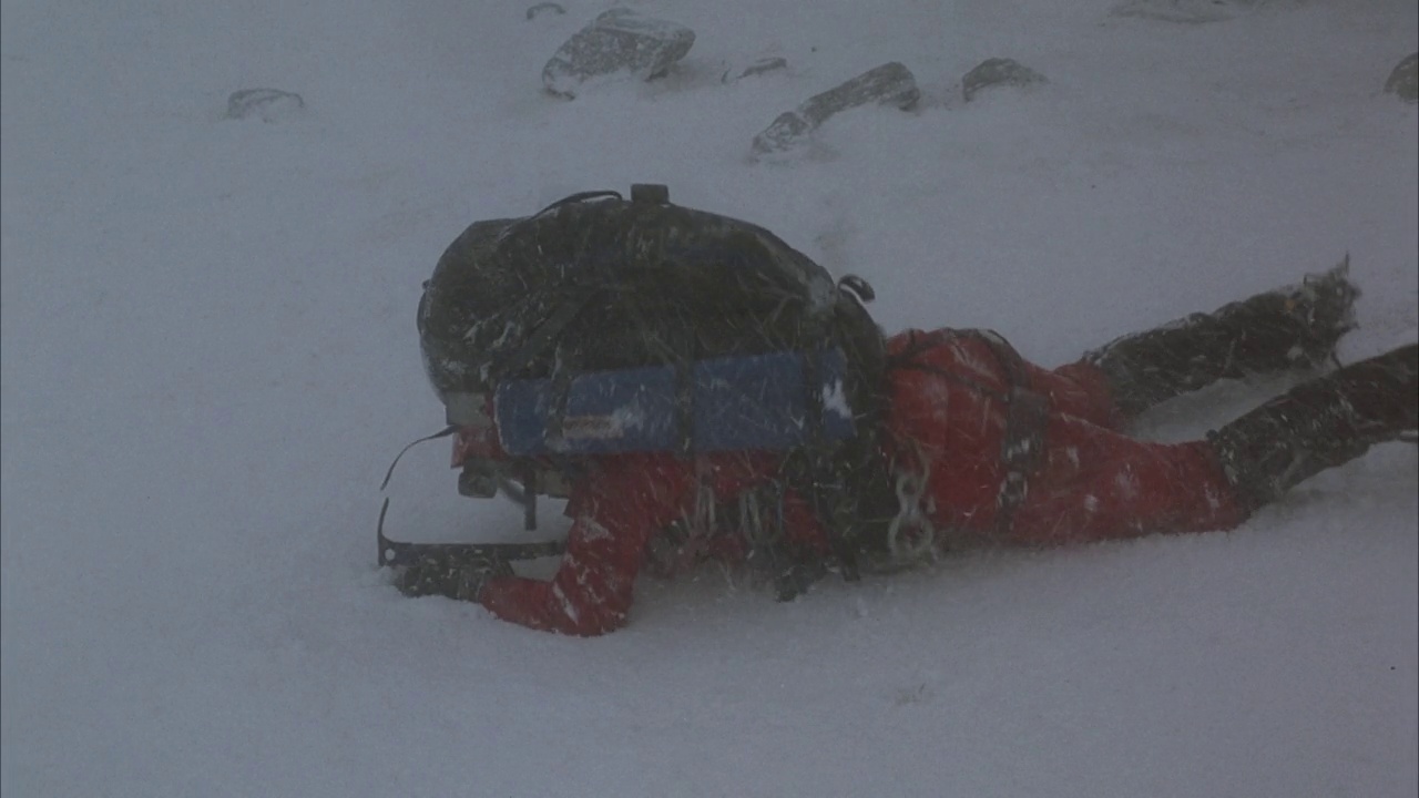 中等角度下的登山者带着背包和鹤嘴锄在暴风雪中从右到左爬行。看到脚下的积雪融化登山者掉进了一个裂缝。看到雪在裂缝口周围吹。看攀登者的绳索视频素材