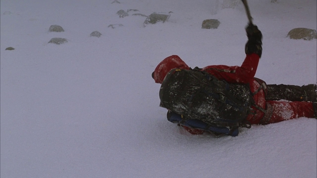 中等角度下的登山者带着背包和鹤嘴锄在暴风雪中从右到左爬行。看到脚下的积雪融化登山者掉进了一个裂缝。看到雪在裂缝口周围吹。看攀登者的绳索视频素材