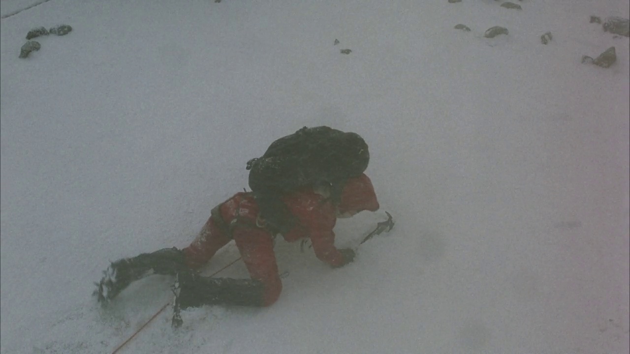 中等角度下的登山者带着背包和鹤嘴锄在暴风雪中从右到左爬行。看到脚下的积雪融化登山者掉进了一个裂缝。看到雪在裂缝口周围吹。看攀登者的绳索视频素材