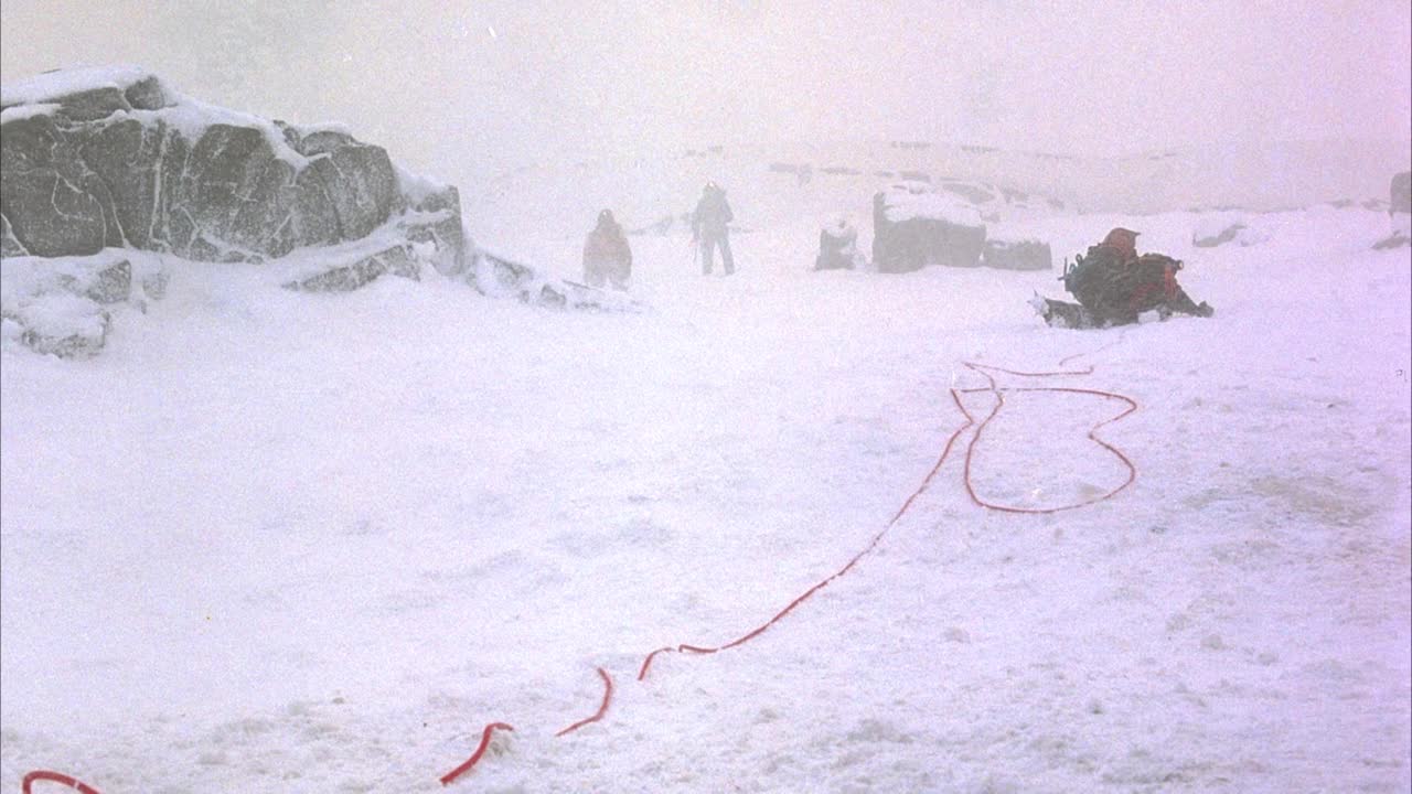 中等角度的登山者徒步穿越暴风雪或暴风雪在大雪覆盖的巨石。见第一个攀登者膝上系红绳。看到红色的绳子被拉紧，攀登者被拖向pov停了下来。行动。视频素材