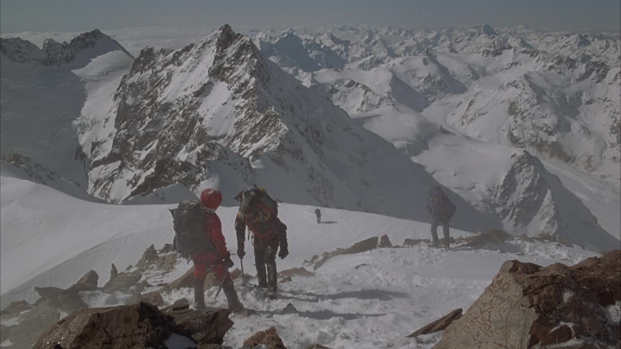 中等角度的登山者徒步穿越斜坡或丘陵在中等降雪。看前面两个攀登者面对面。可以说话。看到登山者转向远离pov，开始在雪地上徒步旅行，偶尔会转弯。能帮到别人吗视频素材