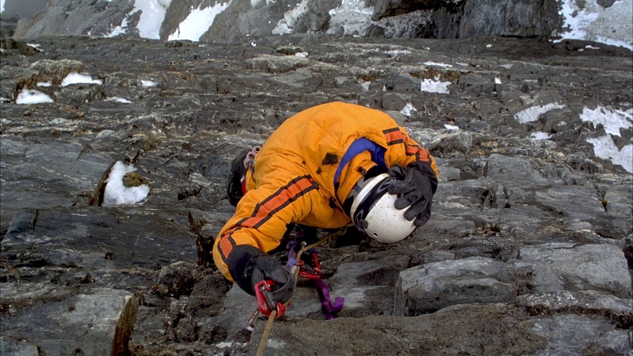 登山者在多岩石的山坡上以高角度下山。见登山者将装备包推出框架和盖头。看到岩石和碎片落在登山者身上。看山腰和背景上的雪。视频素材