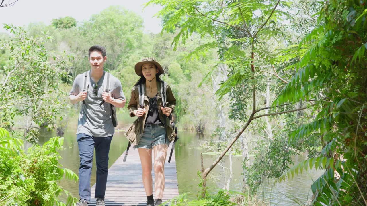 亚洲男人和女人背包客朋友一起在森林里旅行。迷人的年轻夫妇在夏天的假期旅行中散步和探索自然木材的幸福和乐趣。视频素材