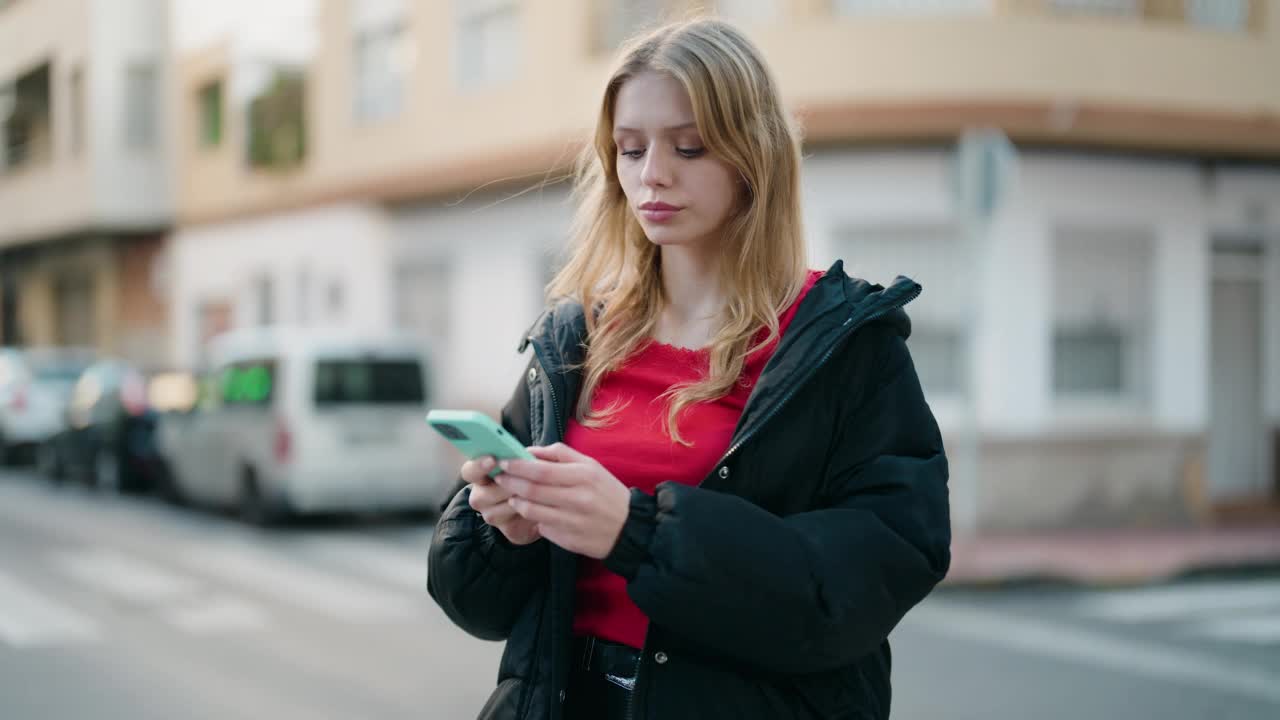 年轻的金发女孩微笑自信地使用智能手机在街上视频素材