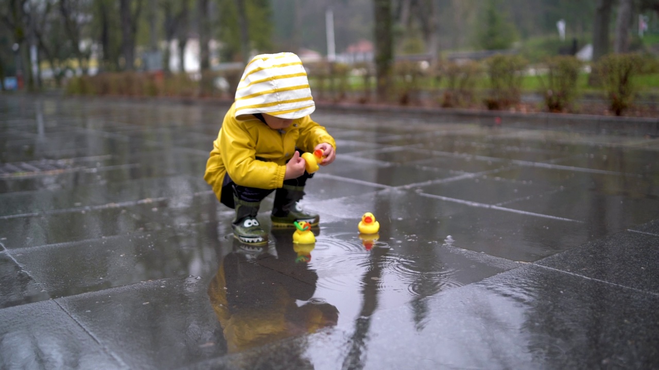 美丽有趣的金发蹒跚学步的男孩和橡皮鸭，在雨中玩视频素材