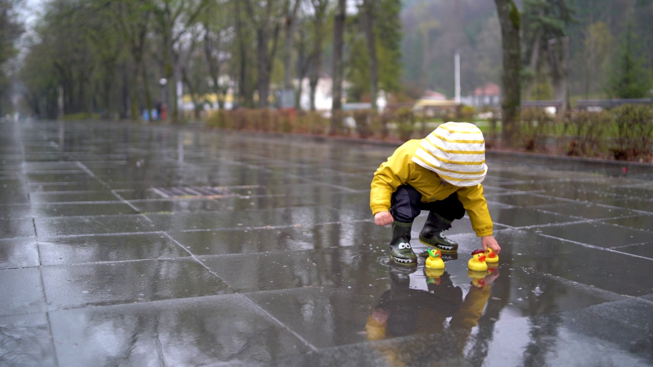 美丽有趣的金发蹒跚学步的男孩和橡皮鸭，在雨中玩视频素材