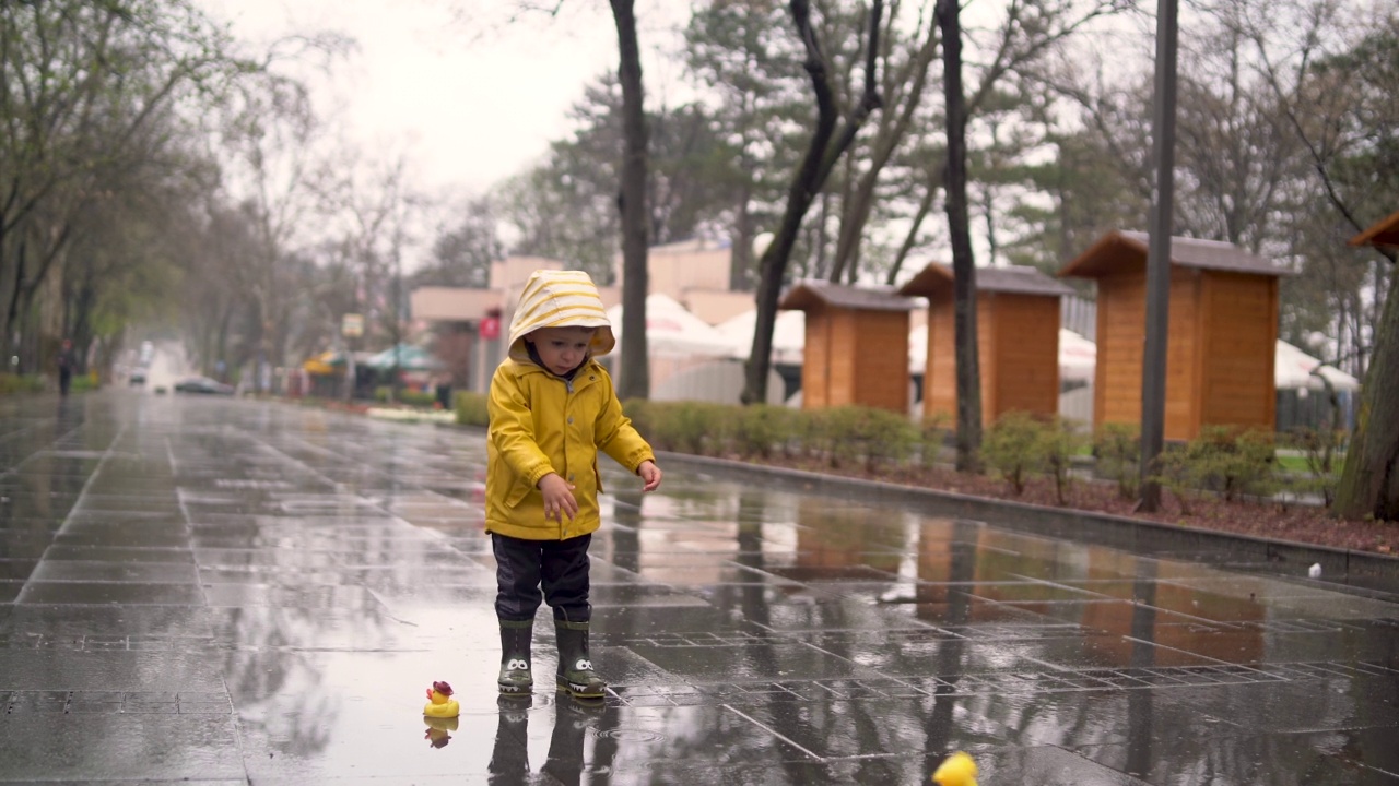 美丽有趣的金发蹒跚学步的男孩和橡皮鸭，在雨中玩视频素材