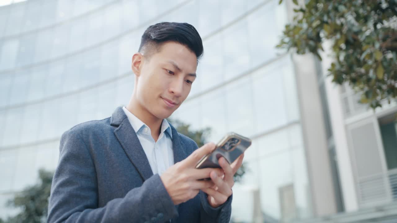 一个快乐的商人站在城市里，用着智能手机。一个自信的年轻商人，在城市背景下在网上工作视频素材