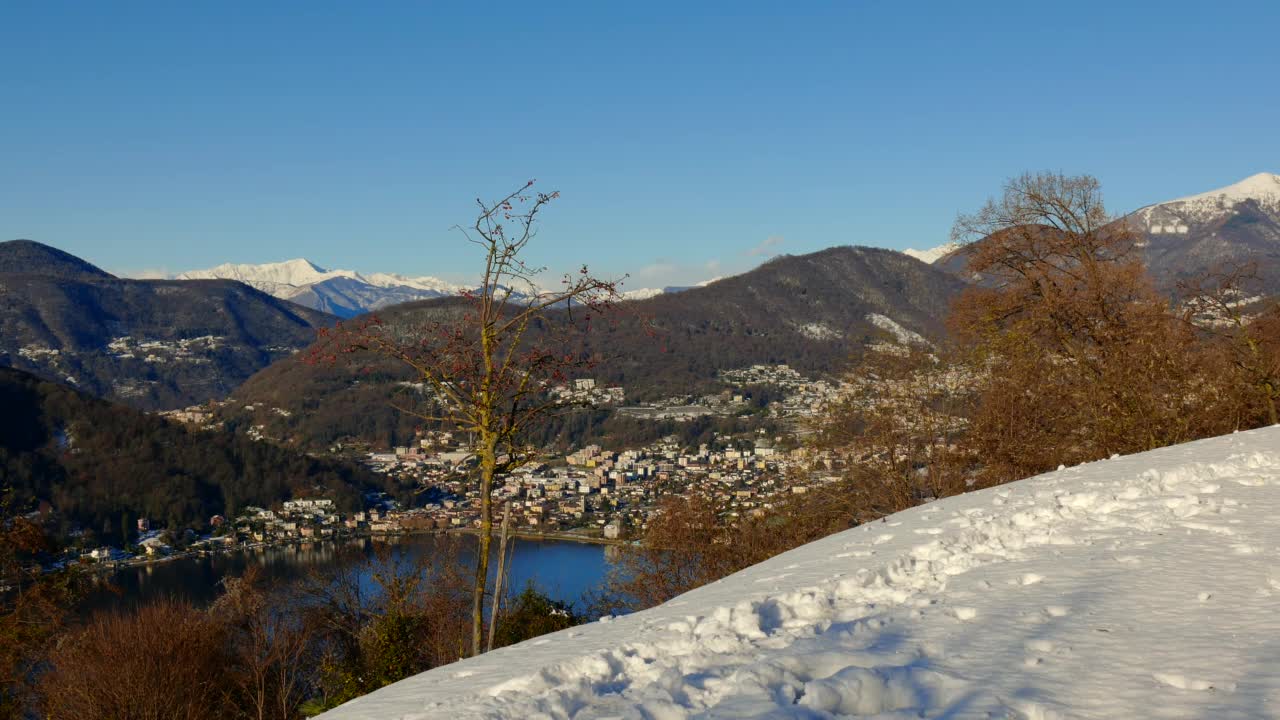 优雅的男人在智能手机和喜悦山景与卢加诺湖与雪和晴朗的蓝天在晴朗的日子与卡斯拉诺市的看法视频素材