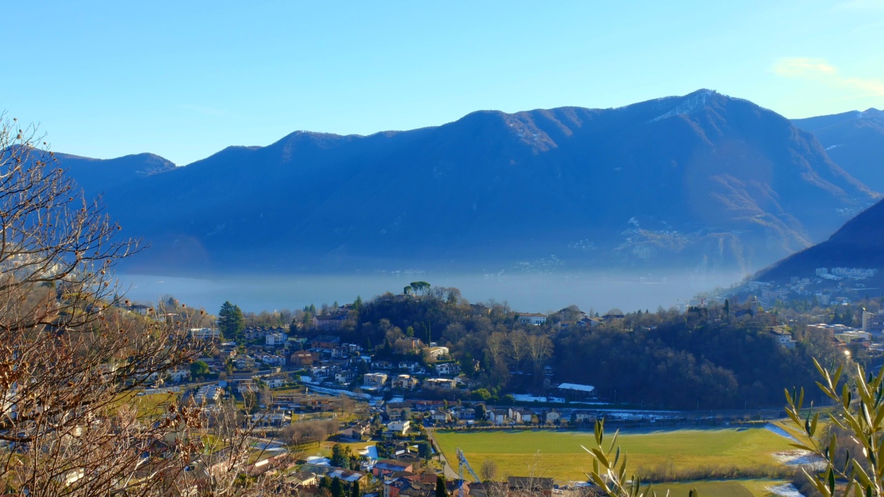 阳光明媚的卢加诺湖的山景和卢加诺的城市风景视频素材