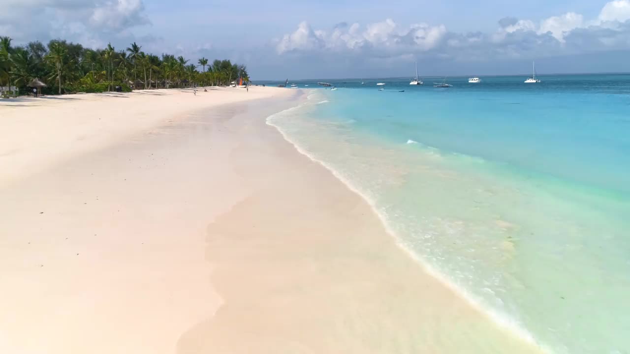 夏天日落时分，鸟瞰海浪、绿色的棕榈树、沙滩、清澈湛蓝的海水中的船只。无人机俯视图。印度洋。去非洲的桑给巴尔旅游。丰富多彩的景观视频素材