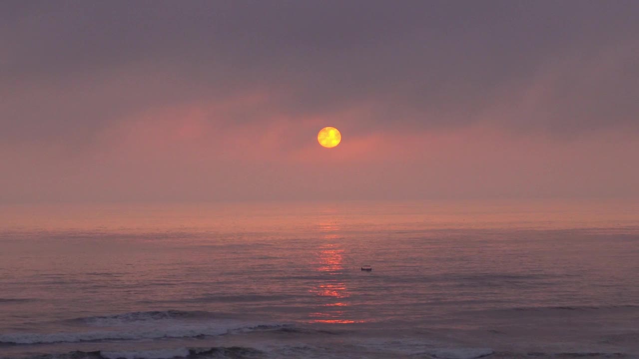 一个美丽的日落，圆圆的黄色的太阳在海上，一艘船漂浮在海滩上的海浪和海鸥飞行在4k视频素材